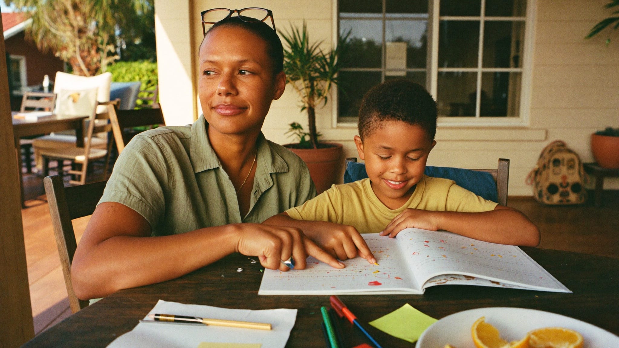 An educator and a young student reading a workbook together at a sunny porch table